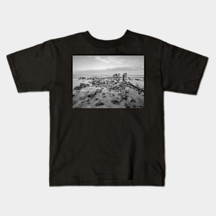 Seaweed covered rocks a the sandy beach Kids T-Shirt